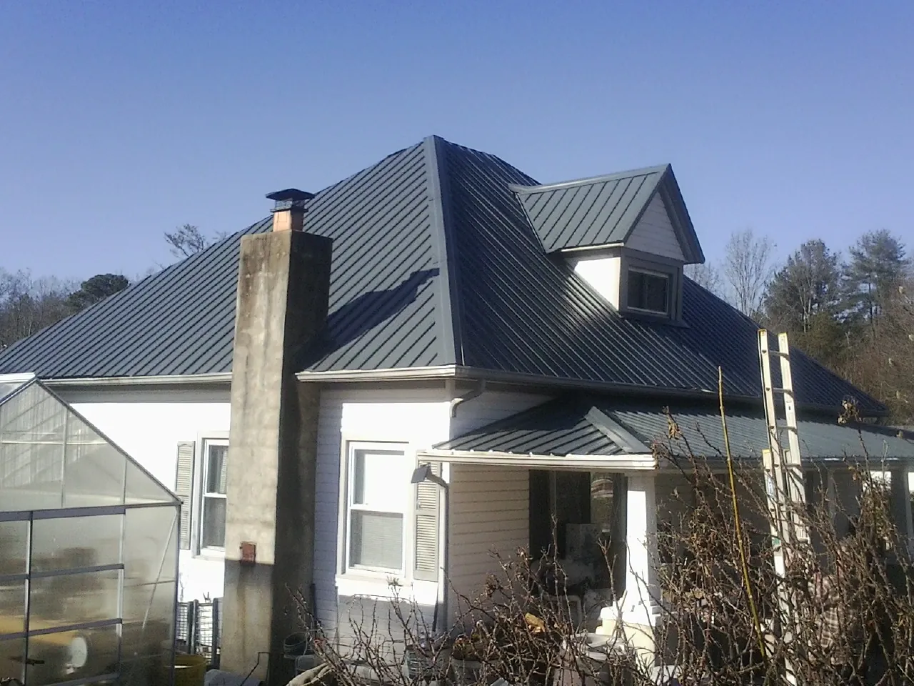 Dark blue standing seam metal roof on a white farmhouse with dormer — Slate & Tile Roof Repair by Roofing Brothers in Neshkoro