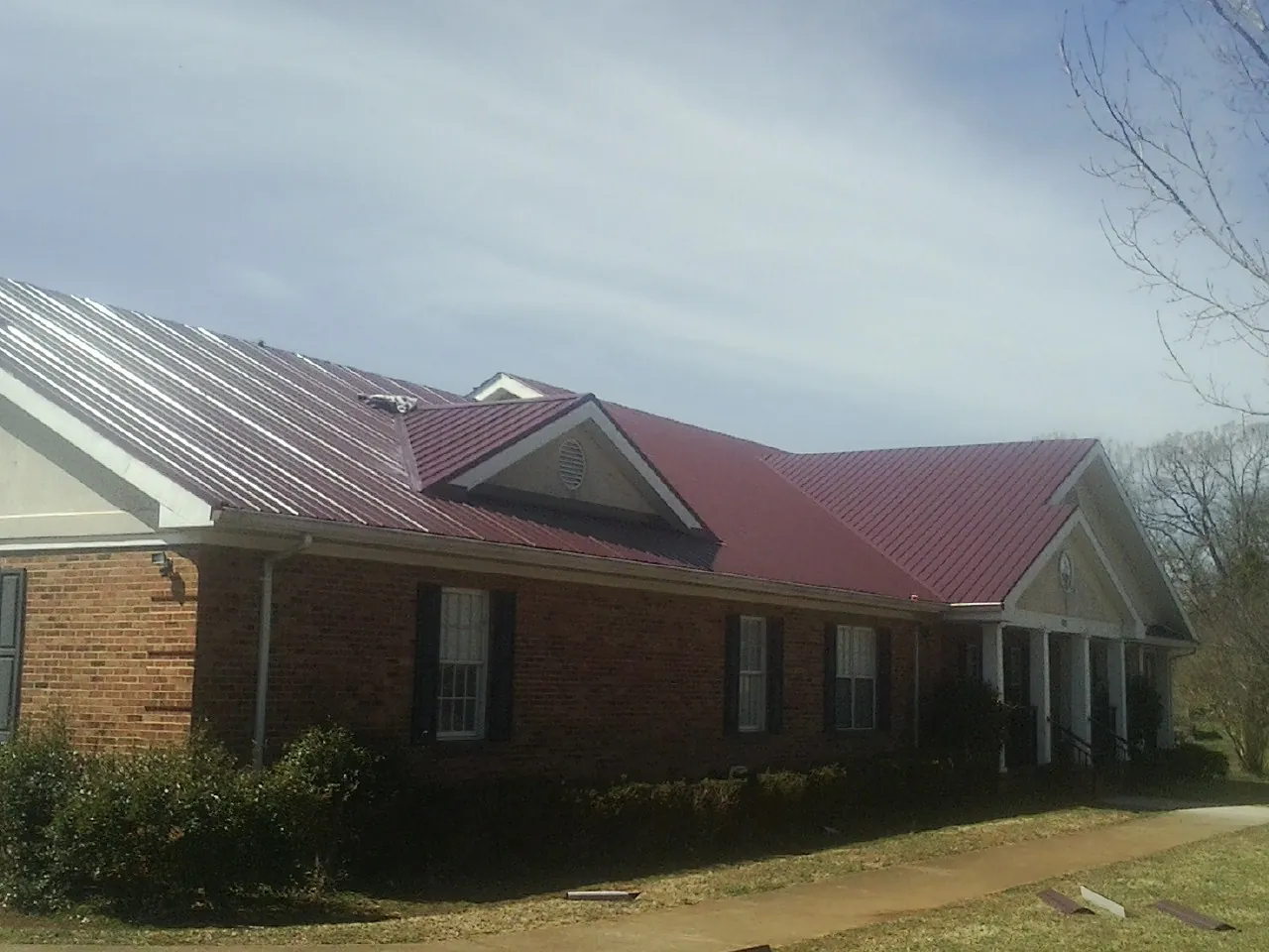 Red metal roof with gabled entries on a long brick building, from a Hail Damage Roof Repair job in Neshkoro