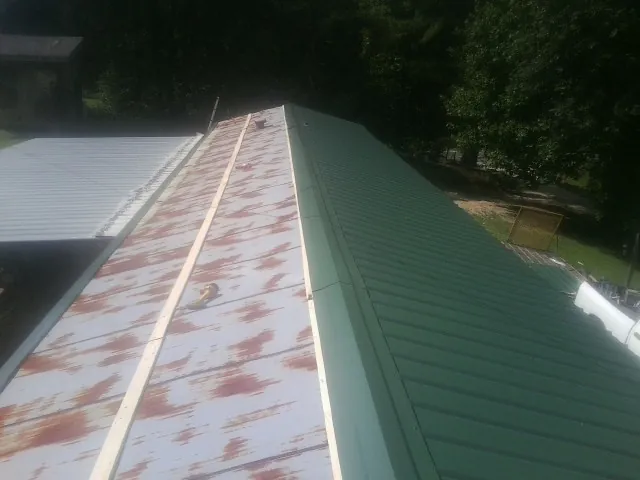 Old rusted panels beside newly installed green metal roofing — Wind Damage Roof Repair by Roofing Brothers in Neshkoro