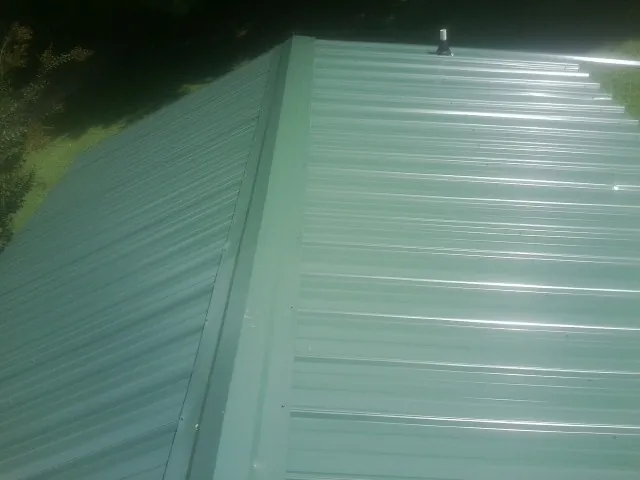 New green metal panels meeting at the ridge of a roof — Flat Roof Repair work by our crew in Neshkoro