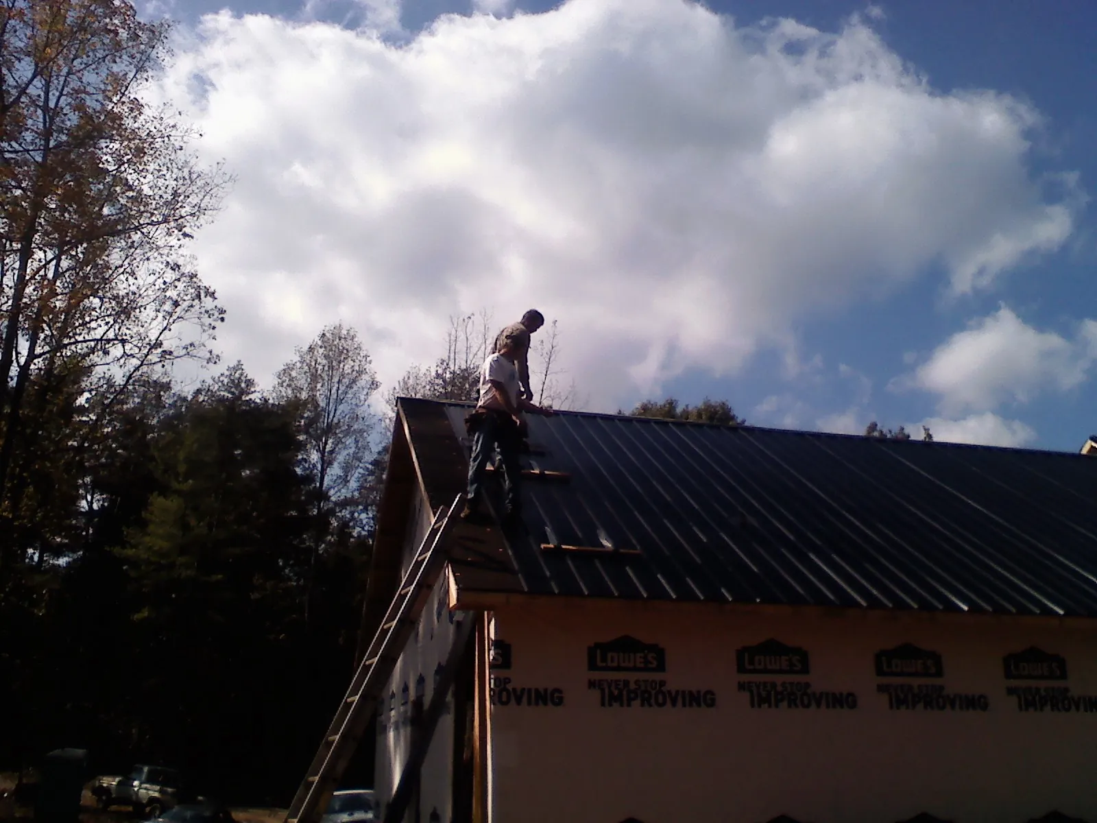 Roofer fastening dark metal panels high against a cloudy sky, from a Roof Inspection job in Neshkoro