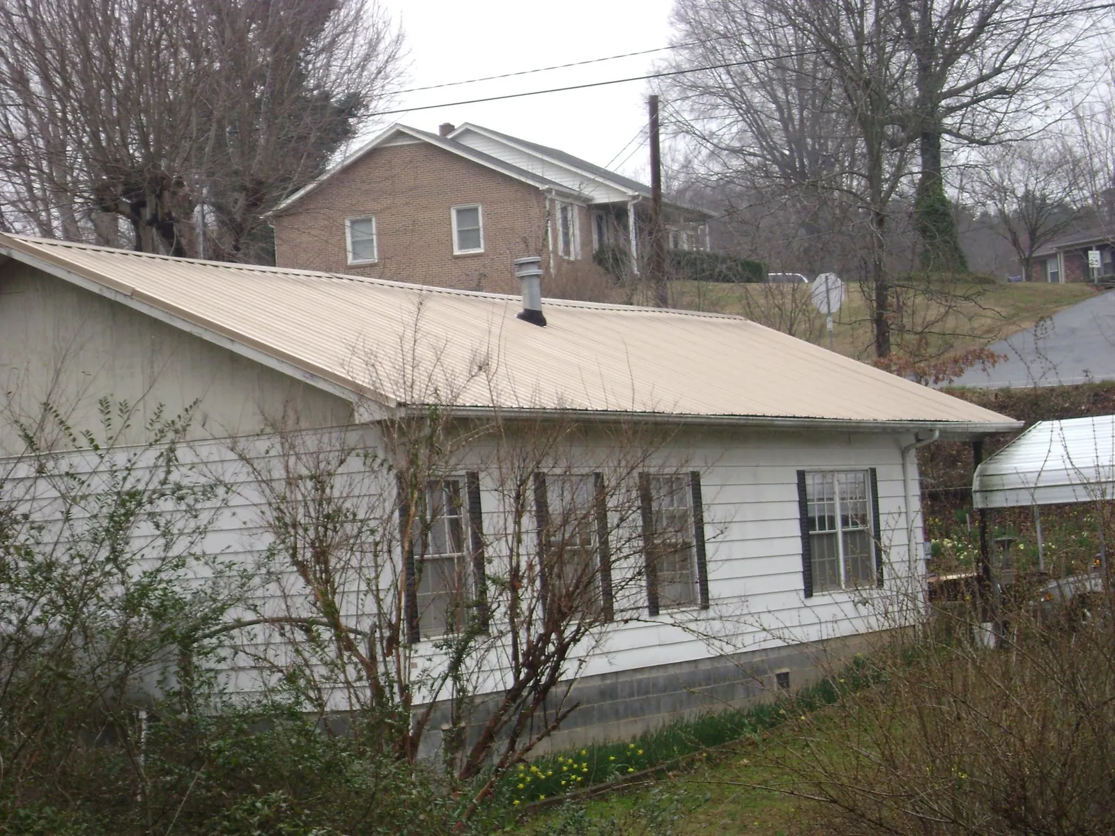 Tan metal roof on a white sided house set into a hillside — Commercial Roofing by Roofing Brothers in Neshkoro