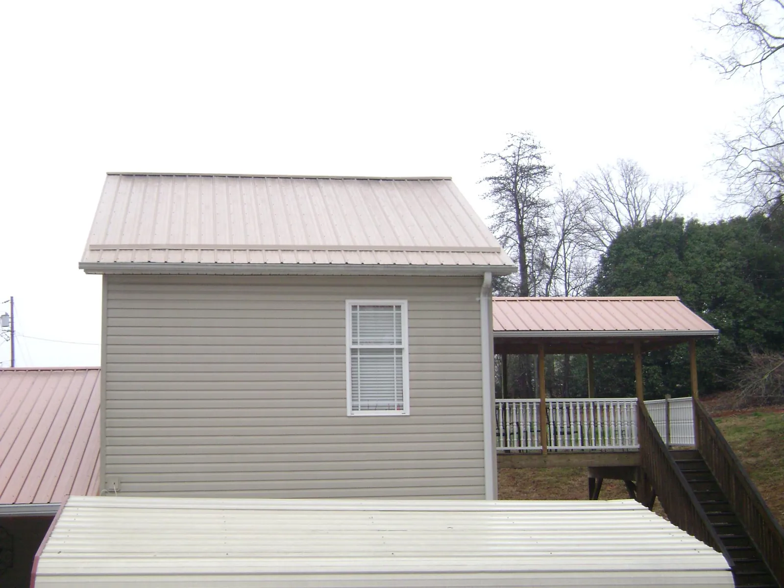 Tan metal roofs on a two story addition and attached porch, from a Roof Replacement job in Neshkoro